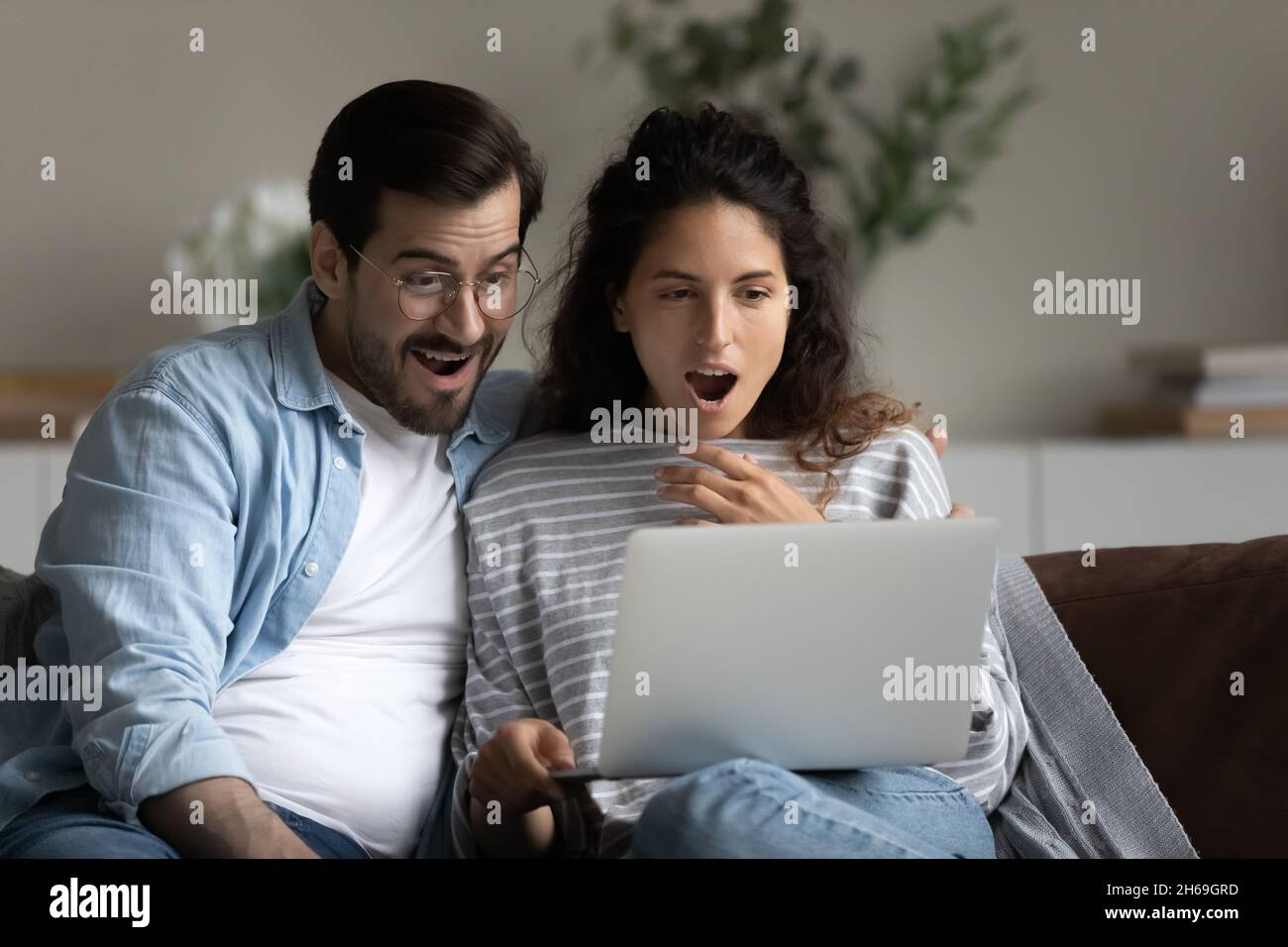 Un jeune couple choqué et débordant de joie à regarder sur un ordinateur portable, à lire des nouvelles étonnantes Banque D'Images