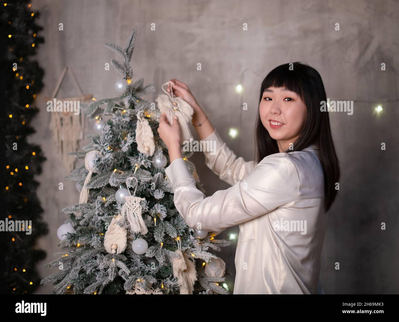 Une jeune, belle femme coréenne asiatique habille un arbre de Noël avec des jouets en macrame naturel dans le style de zéro déchet à la maison avec positif Banque D'Images