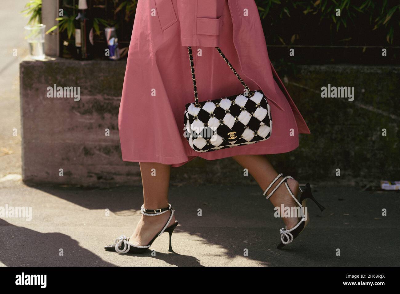 Milan, Italie - 24 septembre 2021: Tenue de style de rue, femme à la mode portant un long manteau rose, un sac à main à carreaux noir et blanc de Chanel, b Banque D'Images