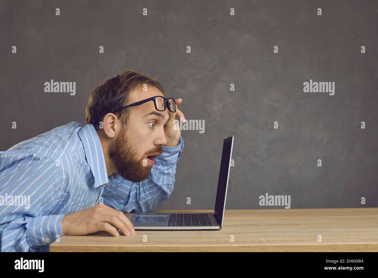 Vue latérale d'un homme avec une expression surprise assis à une table et regardant un écran d'ordinateur portable. Banque D'Images