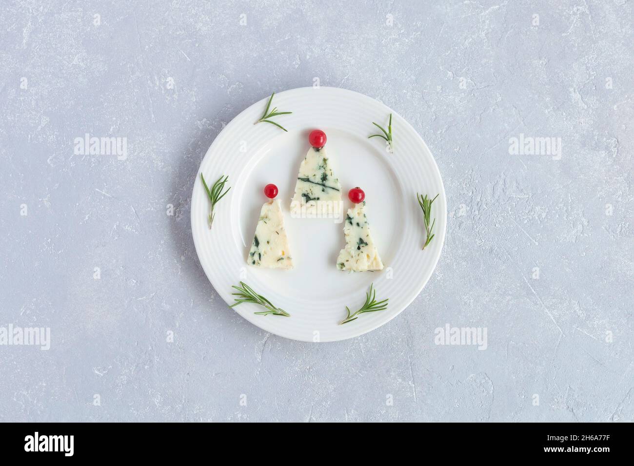 arbres du nouvel an fabriqués au fromage roquefort et décorés de raisins de corinthe rouges, sur une assiette, fond gris, vue de dessus Banque D'Images