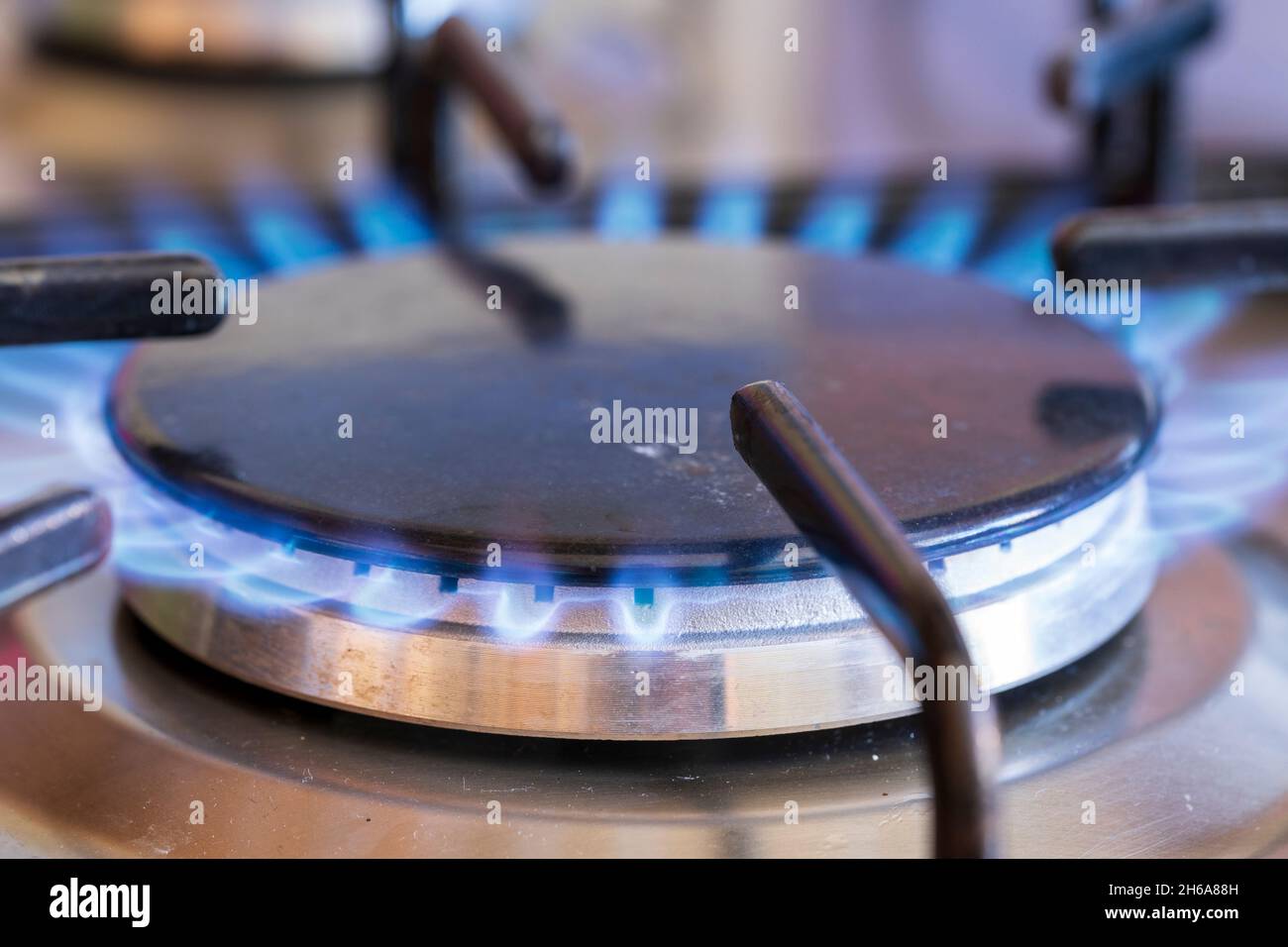 Anneau à gaz allumé sur la table de cuisson à gaz.Anneau circulaire gris recouvert d'un dessus noir en fonte, flammes bleues provenant des évents à gaz sur le côté de l'anneau. Banque D'Images