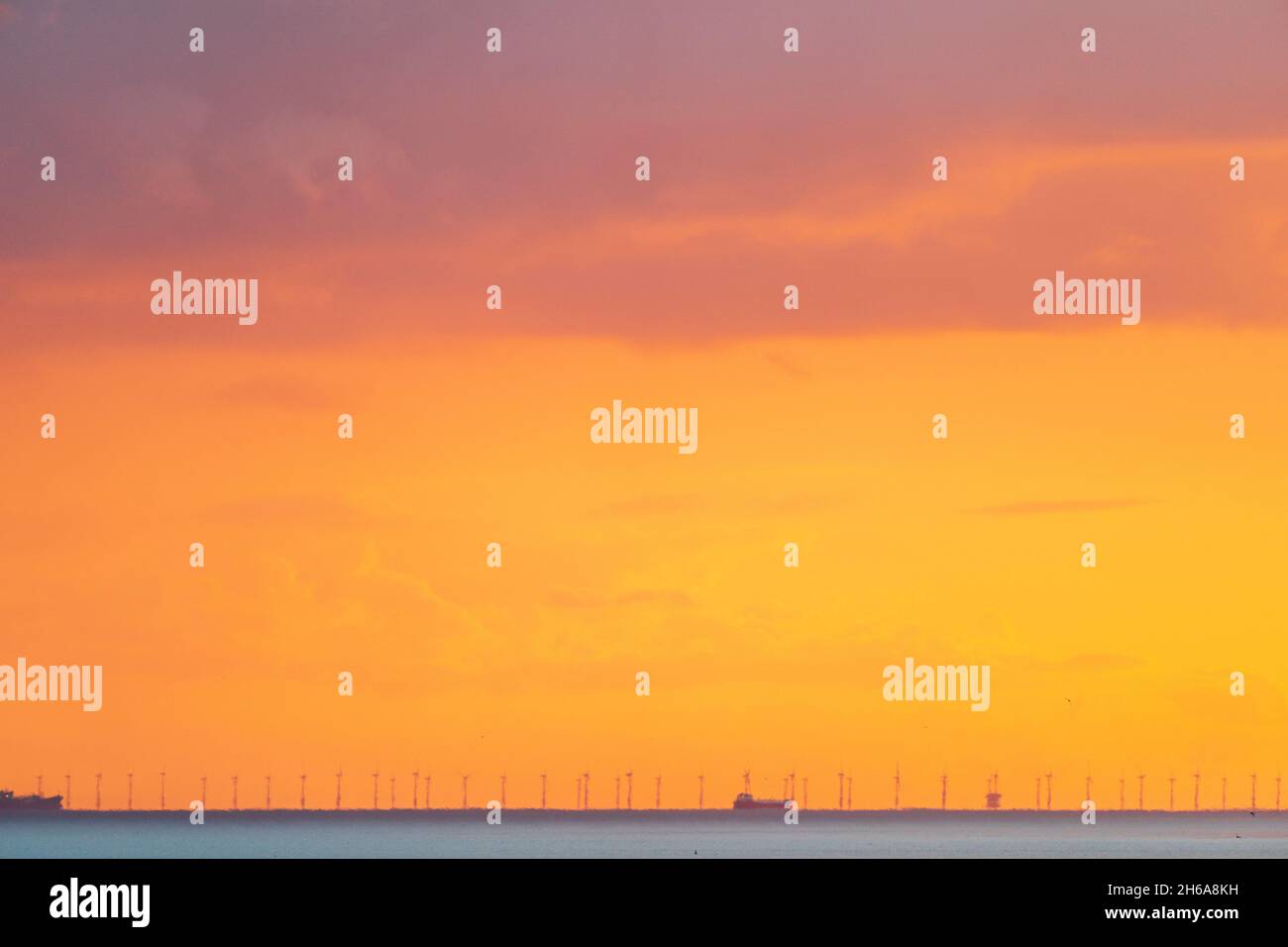 Manche avec un ciel jaune nuageux au lever du soleil, un horizon bas, des navires de cargaison et des éoliennes d'un parc éolien offshore vu par une forte brume de chaleur. Banque D'Images