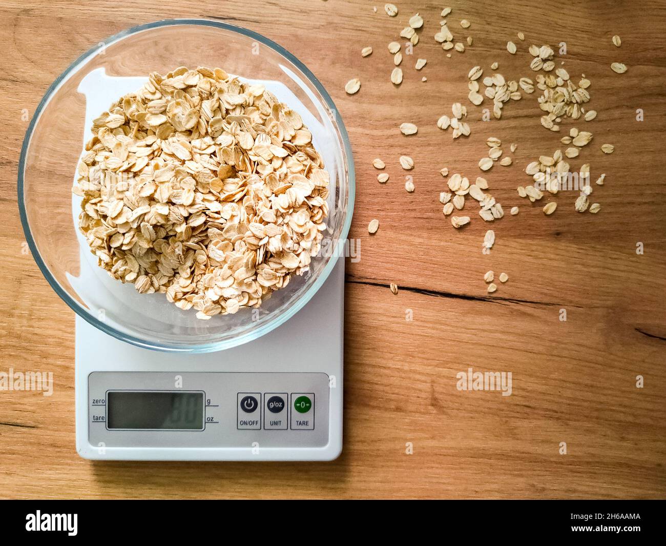 Gruaux d'avoine, gruaux pesant dans un bol en verre sur des balances électroniques de cuisine sur une table en bois. Banque D'Images