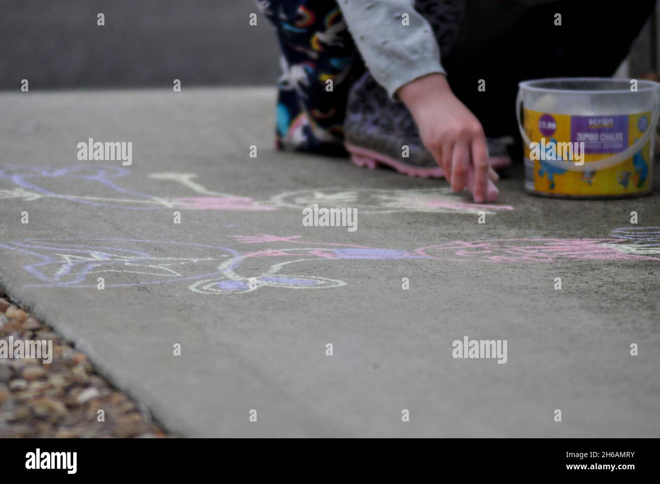Enfant utilisant des craies jumbo pour tirer dehors sur le béton Banque D'Images
