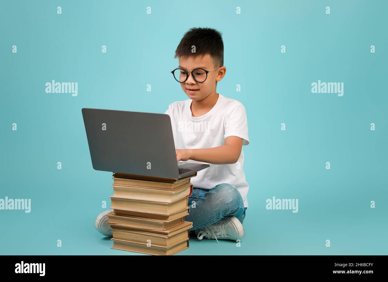 Concept d'apprentissage à distance.Adorable écolier asiatique en lunettes à l'aide d'un ordinateur portable placé sur la pile de livres, Smart Korean Kid Study en ligne avec l'ordinateur, STIT Banque D'Images