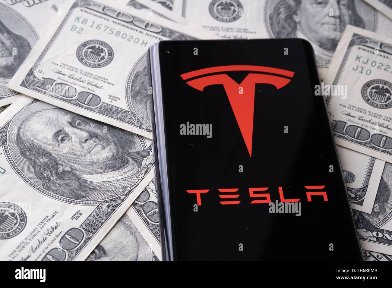 Logo de la société Tesla vu sur le smartphone placé sur la pile de dollars de nous.Concept.Stafford, Royaume-Uni, 14 novembre 2021. Banque D'Images