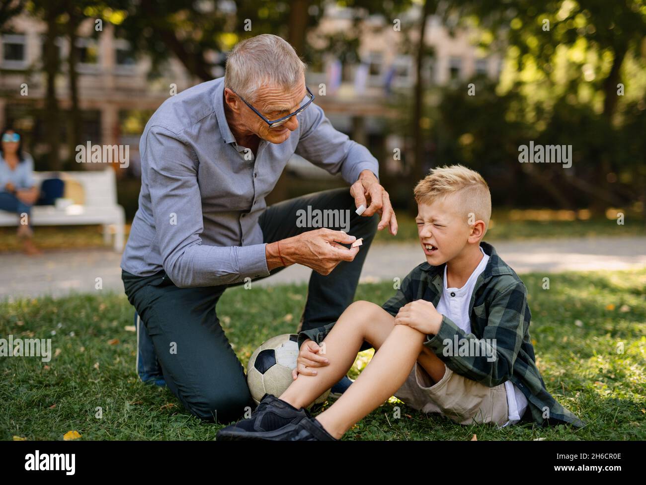 Petit garçon avec des pleurs de jambe blessés, son grand-père lui donne du plâtre à l'extérieur dans le parc. Banque D'Images