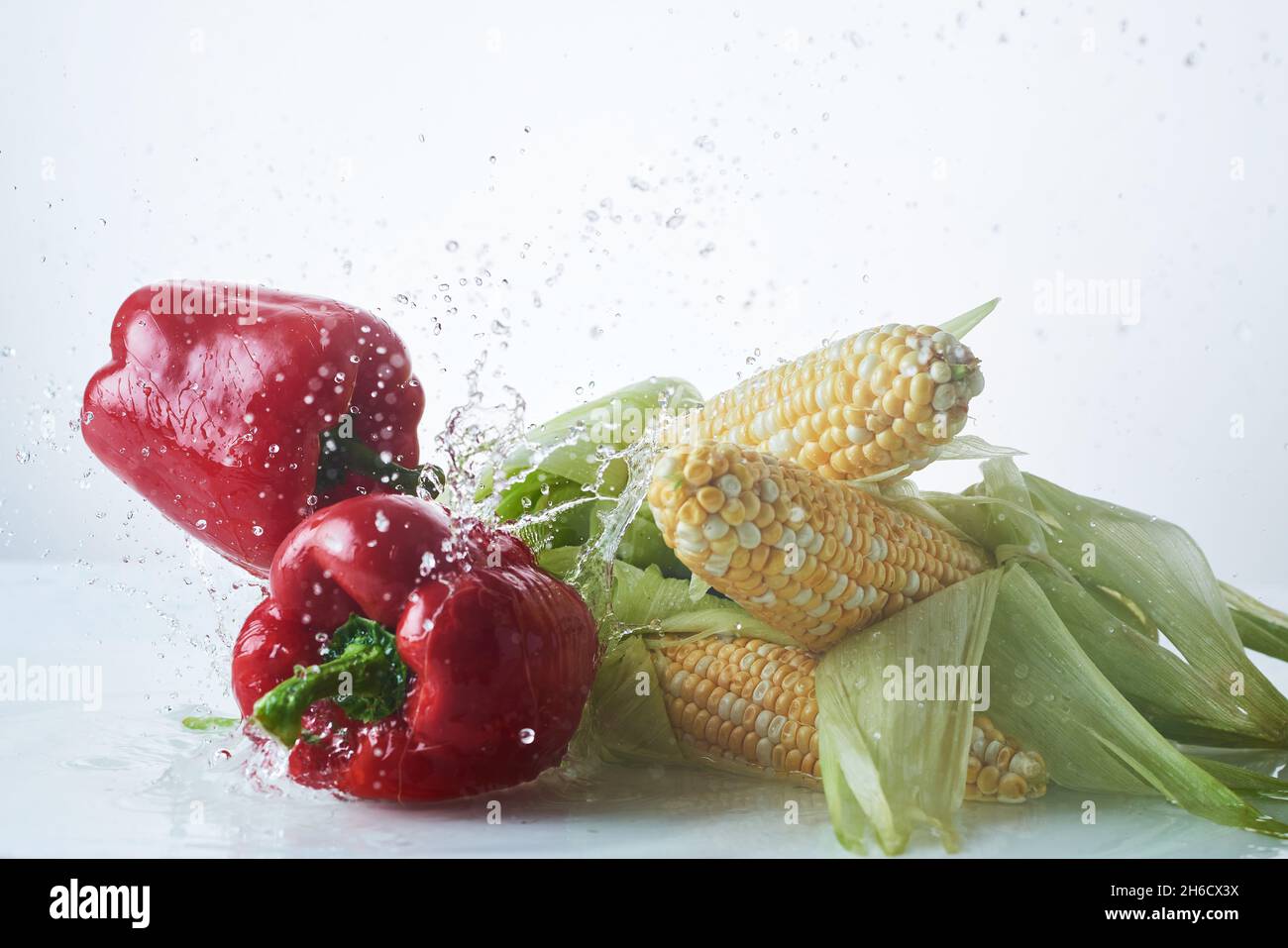 Légumes frais dans des éclaboussures d'eau sur fond blanc, poivrons, maïs sur l'épi. Banque D'Images