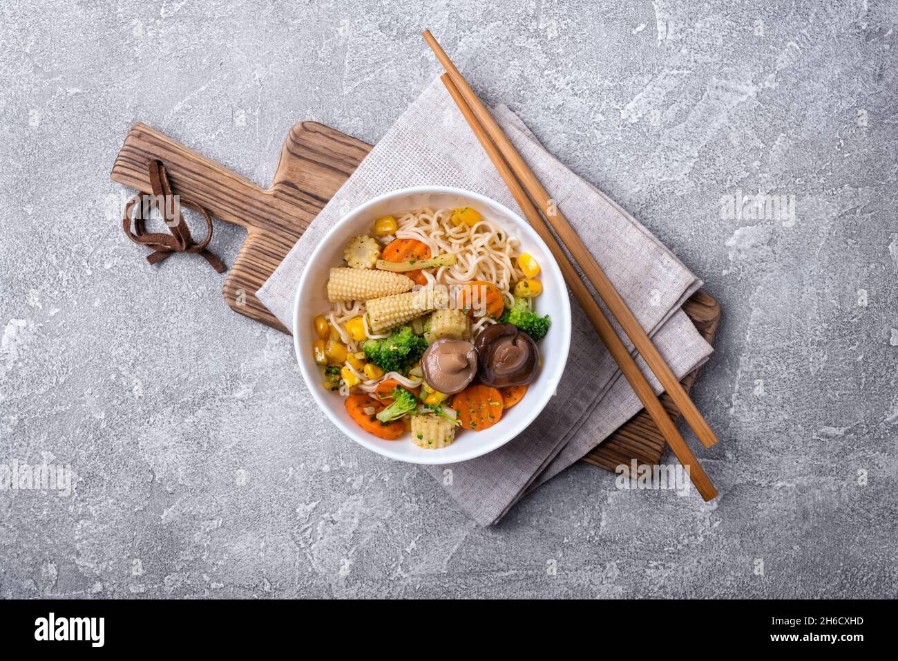 Vue de dessus de l'assiette avec des nouilles asiatiques, du maïs, du brocoli, des carottes et des champignons shiitake sur fond de béton gris Banque D'Images