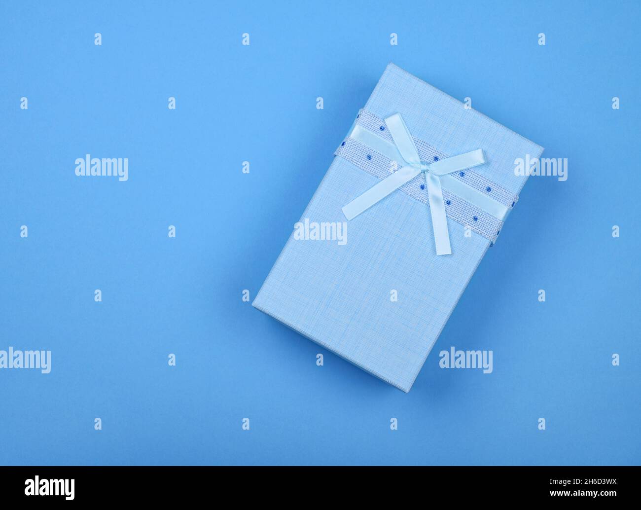 Modèle de Saint-Valentin de boîte-cadeau fermée bleu pastel avec noeud en mousseline sur fond de papier d'emballage bleu, pose à plat rapprochée, vue du dessus en hauteur, d Banque D'Images
