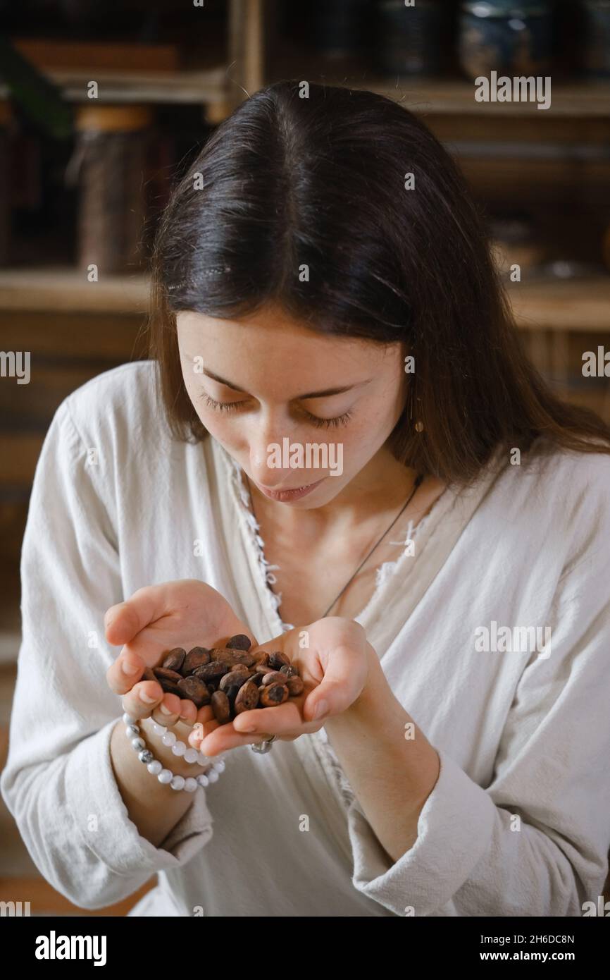 Femme mains tenant des fèves de cacao bio sur table en bois, des nibs de cacao, fabrication artisanale de chocolat dans le style boho rustique pour la cérémonie.Dégustation Banque D'Images