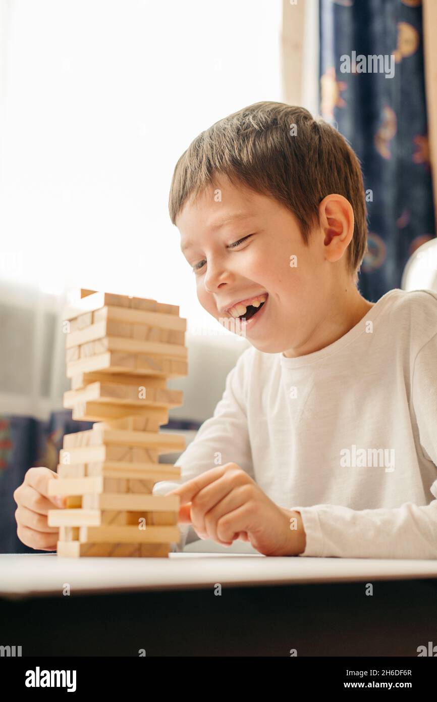 Un garçon caucasien souriant joue à la maison, sur la table à Jenga.Jeux de société pour enfants et adultes.Un passe-temps sans gadgets.Jeux pendant les vacances Banque D'Images