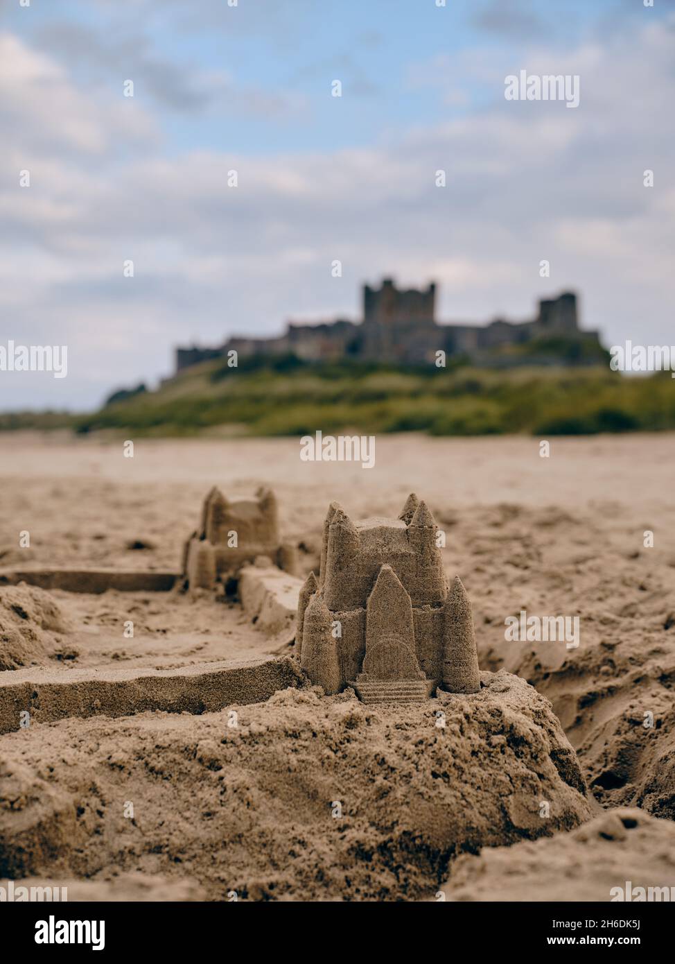 Un château de sable de plage d'été et le château de Bamburgh arrière-plan sur la plage de Bamburgh sur la côte de Northumberland en Angleterre Royaume-Uni - vacances de famille au Royaume-Uni Banque D'Images