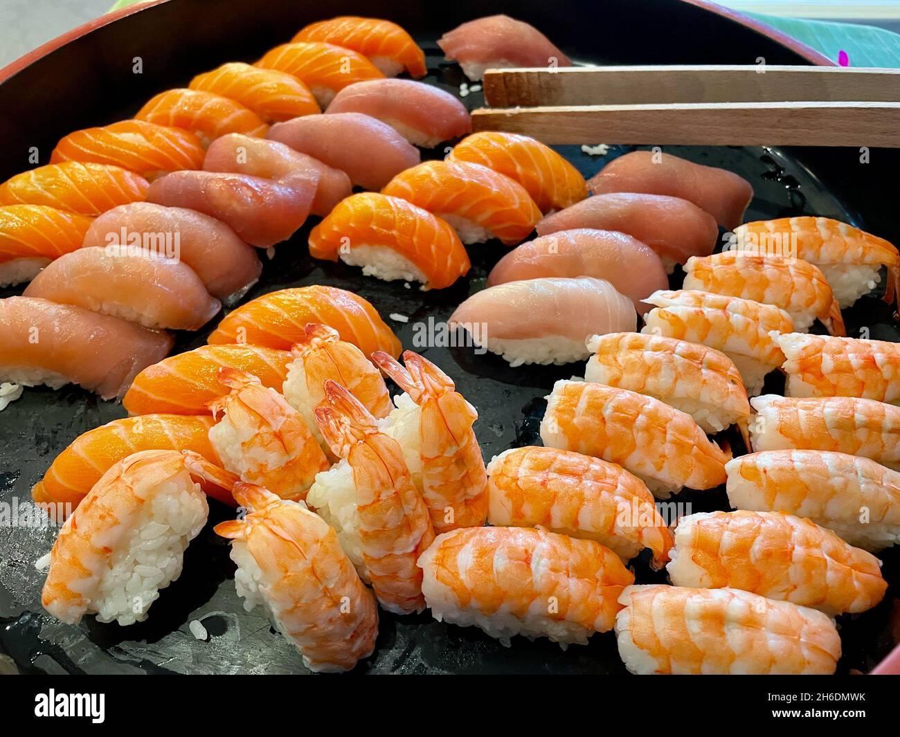 Assortiment de sushis frais, crevettes, thon, babeurre, saumon,sur comprimé noir avec pinces de service en bois.Gros plan. Banque D'Images