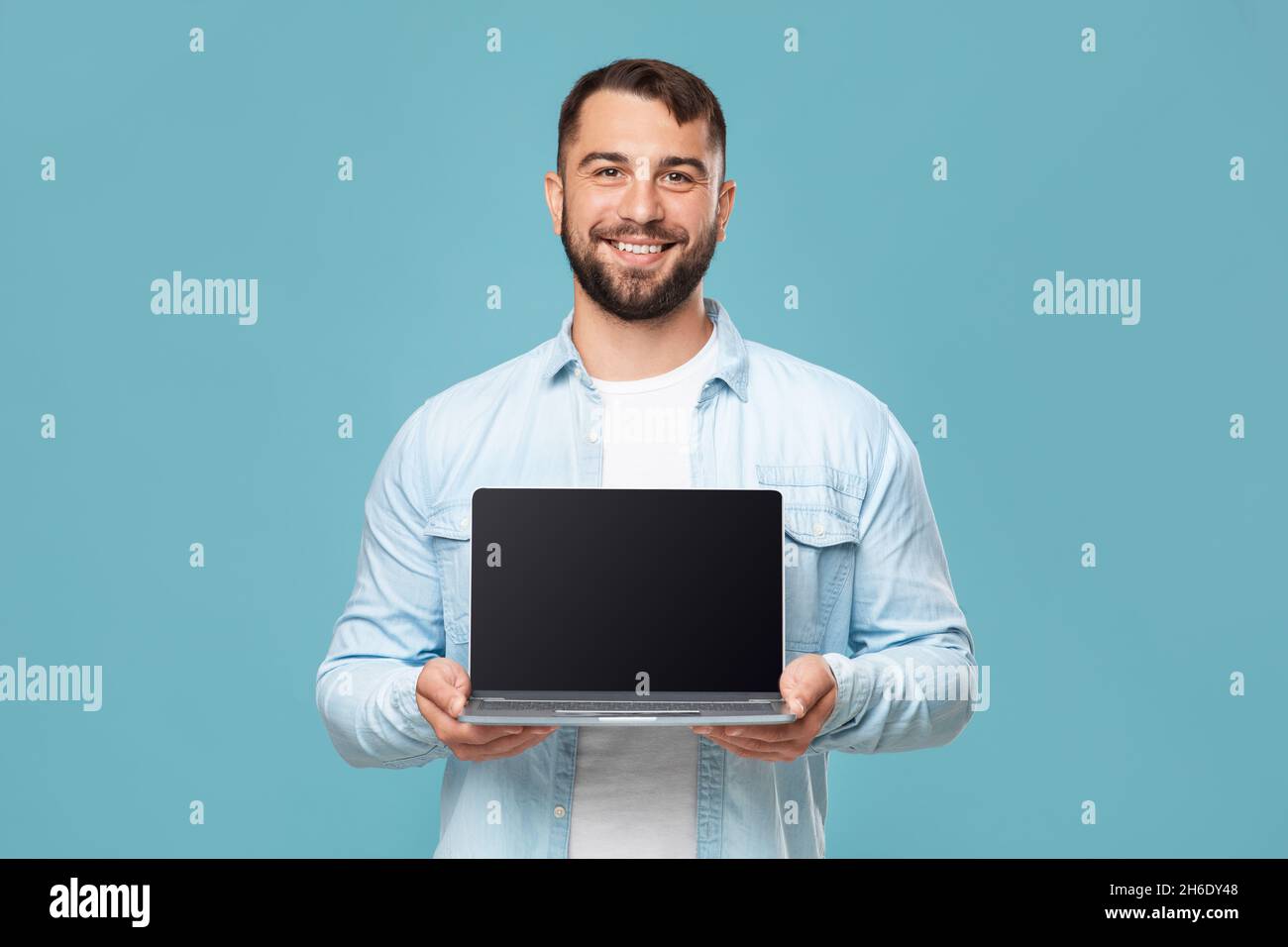 Sympathique heureux adulte européen homme montrant ordinateur portable avec écran blanc, isolé sur fond bleu, espace libre Banque D'Images