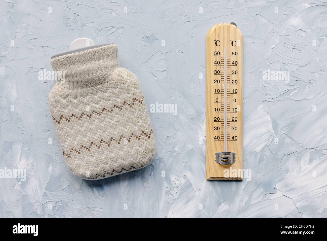 Le thermomètre affiche une température basse et une mini-bouteille d'eau chaude en silicone avec une housse tricotée pour réchauffer les mains ou le corps sur fond blanc et bleu.Maintien au chaud en hiver concept extérieur, espace de copie Banque D'Images