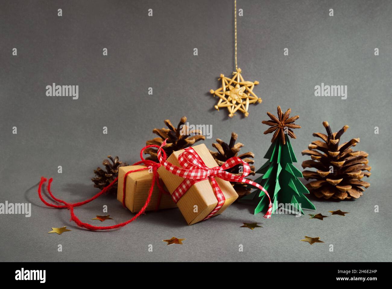 Sapin de Noël origami et boîtes-cadeaux en papier avec rubans rouges, petits cônes et étoiles dorées sur fond gris avec étoile de paille, composition de Noël, Banque D'Images