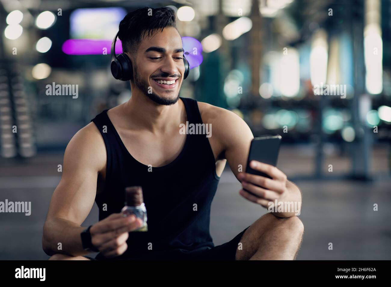 Beau Moyen-Orient Guy utilisant un smartphone tout en se relaxant à la salle de gym après l'entraînement Banque D'Images