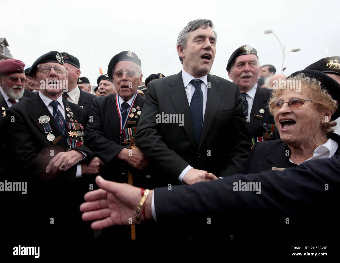 Le Premier ministre britannique Gordon Brown chante le Syne Auld Lang avec des anciens combattants de la guerre de Normandie dans la ville française d'Arromanche, près de l'endroit où les forces britanniques ont pris d'assaut à terre il y a 65 ans, à l'occasion du 65e anniversaire du débarquement. Banque D'Images