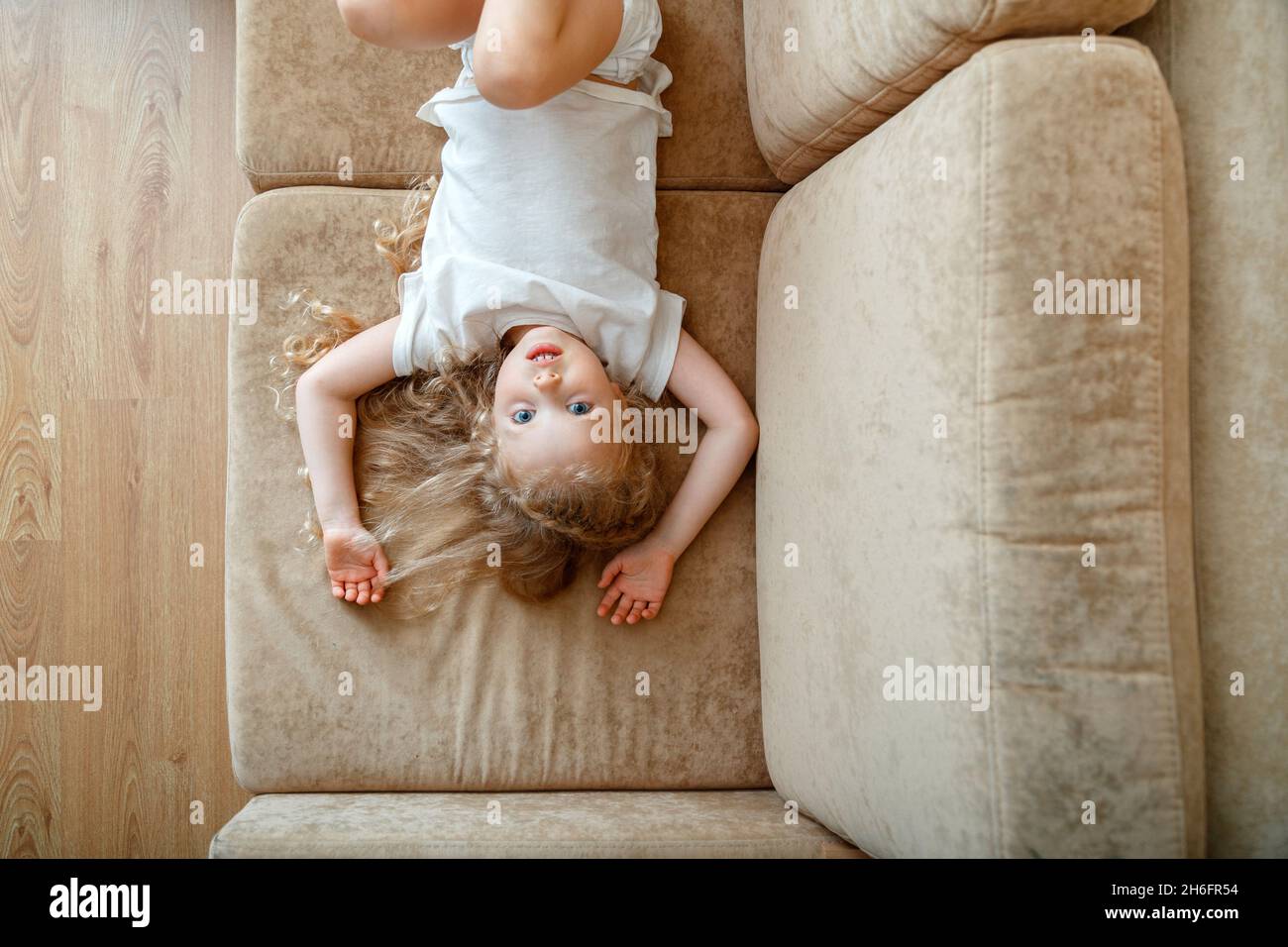 Portrait d'un petit bleu à yeux 5 ans fille enfant enfant avec cheveux bouclés blond allongé sur le canapé.Enfant fille ont des jeux de plaisir allongé sur le canapé dans le salon à Banque D'Images