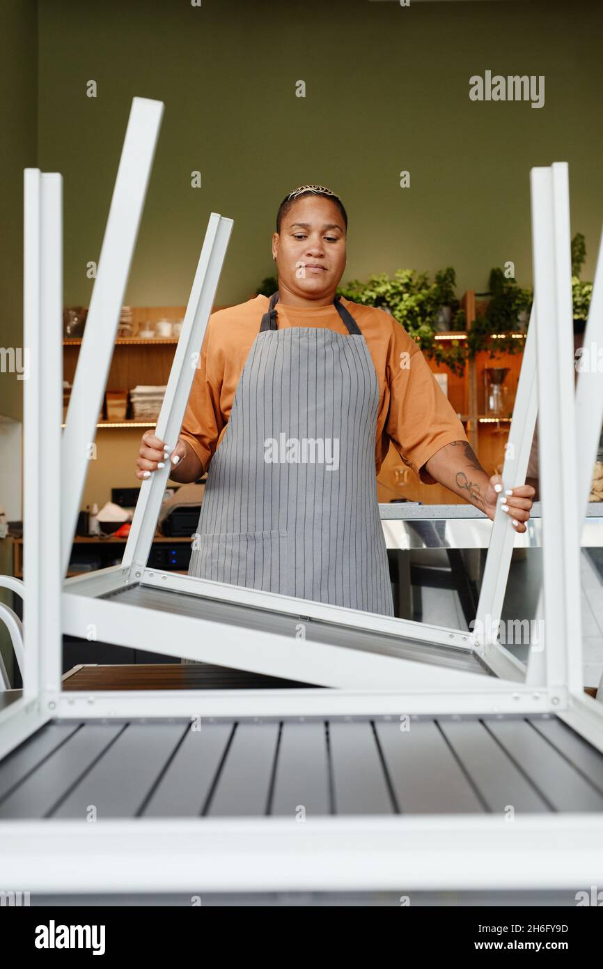 Jeune femme afro-américaine adulte débutant un jour de travail dans un café moderne préparant des tables se retournant et les plaçant Banque D'Images