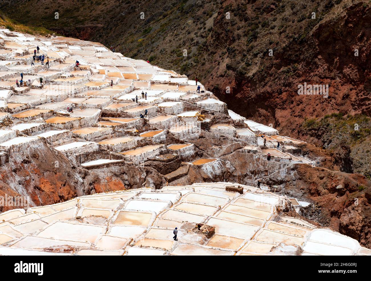 Terrasses salées de Maras avec silhouettes de populations indigènes péruviennes de Quechua faisant la récolte du sel, district de Maras, province de Cusco, Pérou. Banque D'Images