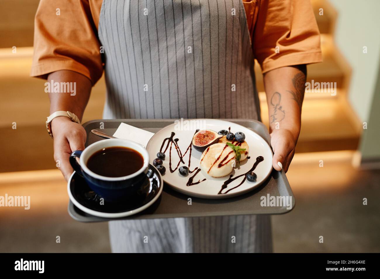 Vue horizontale en grand angle d'une serveuse non reconnaissable travaillant dans un café apportant café et dessert au client Banque D'Images