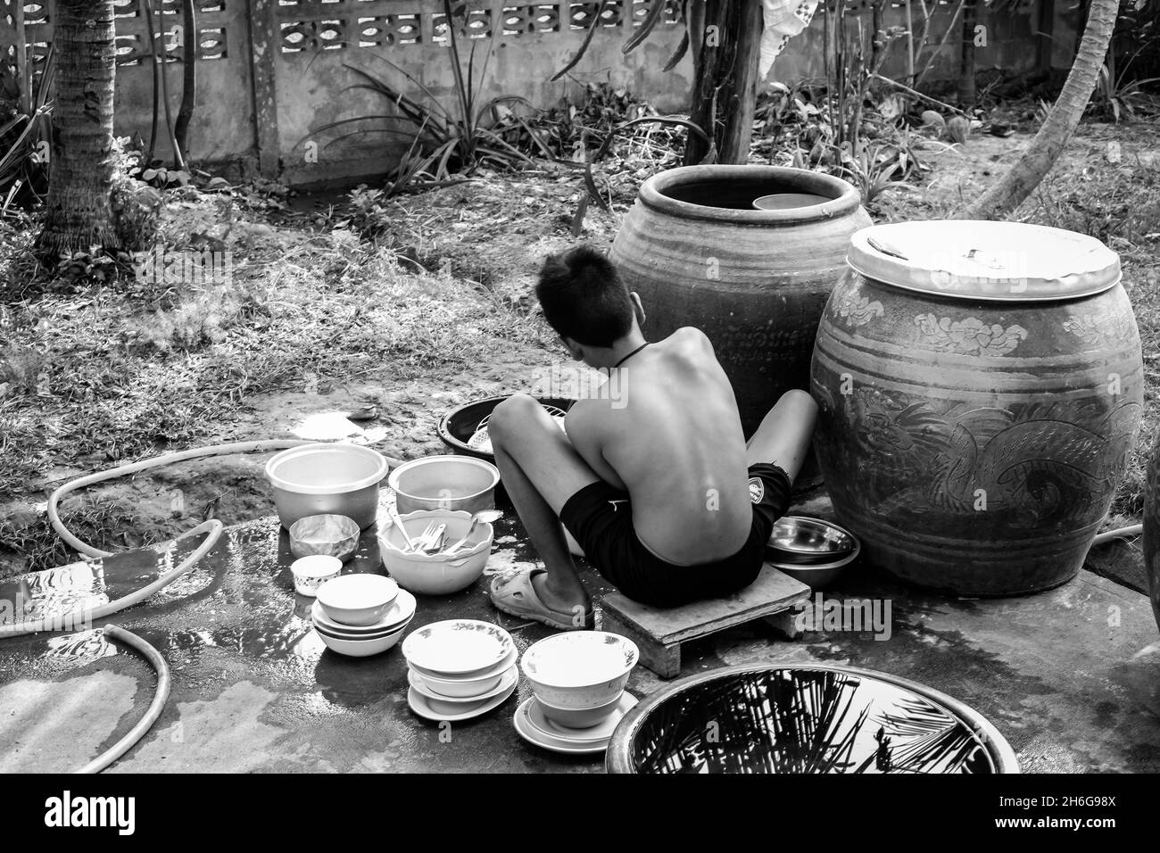 Belle photo d'un enfant en plein air cuisant quelque chose entouré de plats en niveaux de gris Banque D'Images