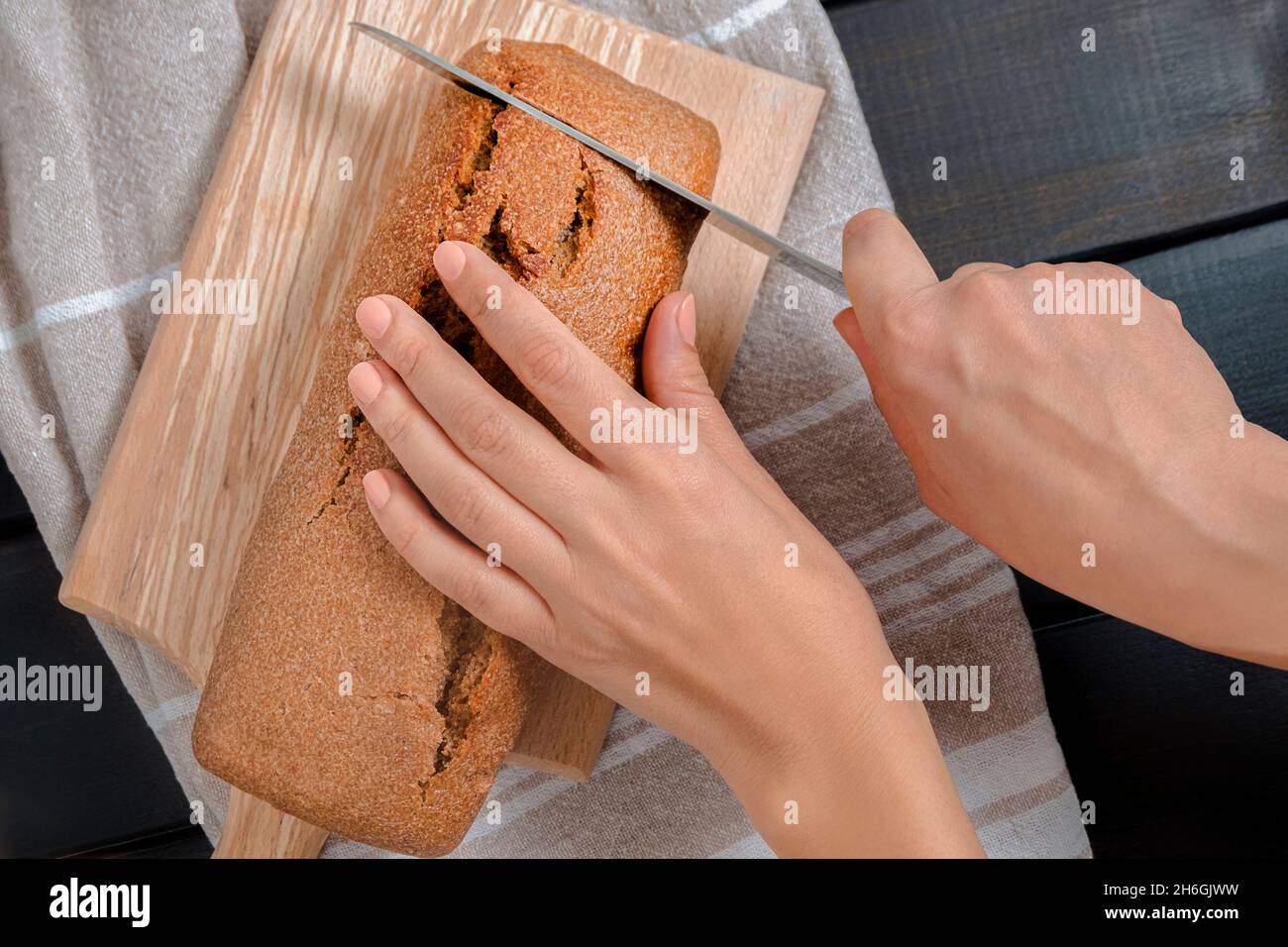 Vue de dessus des mains de femme tenant le couteau et coupant du pain de levain frais sur la planche à découper Banque D'Images