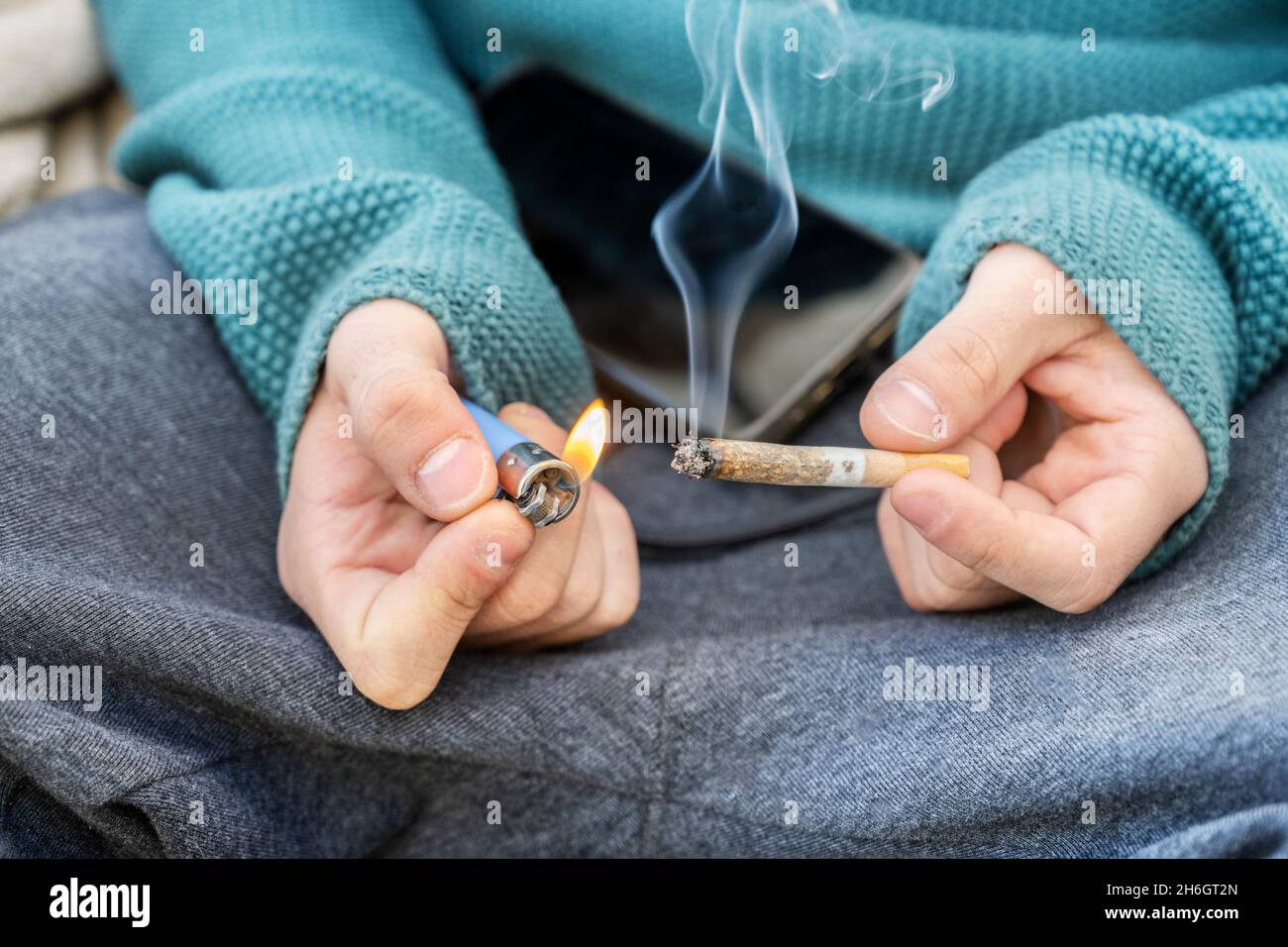 Le jeune homme brûle le papier restant d'une cigarette blonde de tabac avec de la fumée et un mélange d'odeurs ratées Banque D'Images