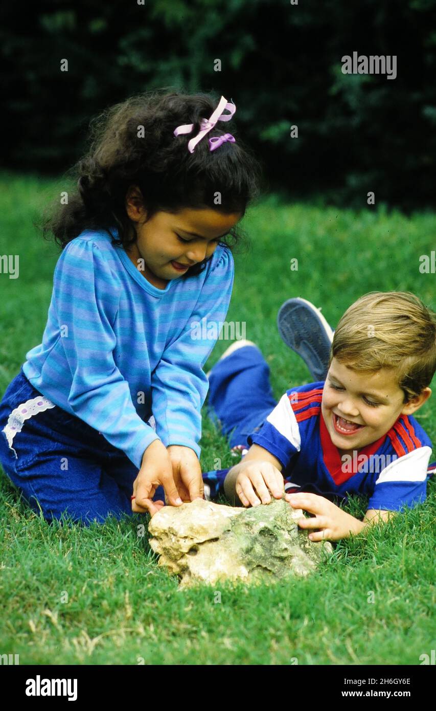 Austin Texas USA, vers 1989: Les enfants de la maternelle inspectent une colonie de fourmis sous un rocher dans un champ herbacé.©Bob Daemmrich Banque D'Images