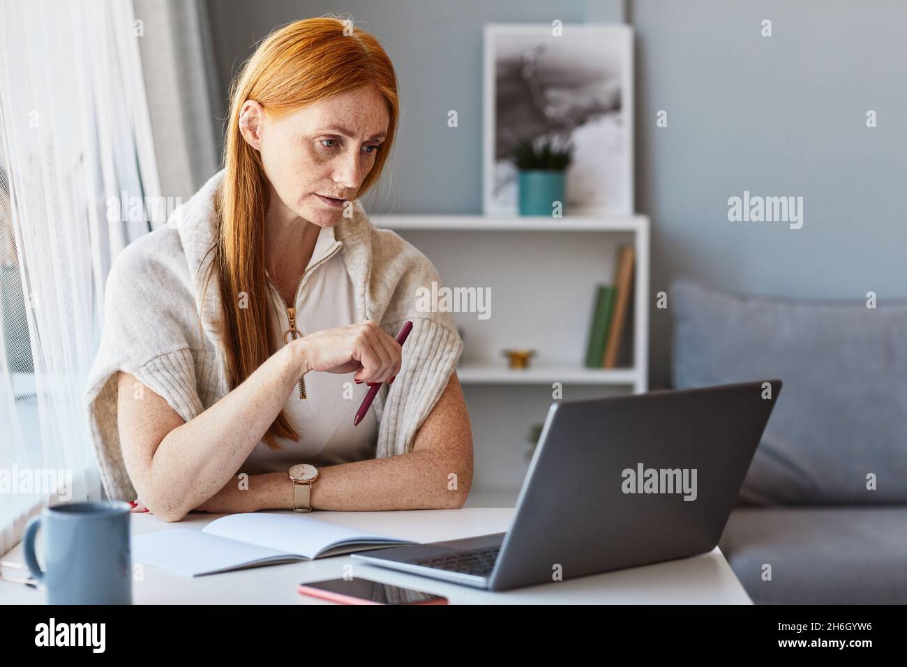 Portrait d'une femme adulte aux cheveux rouges utilisant un ordinateur portable tout en travaillant au bureau à domicile, espace de copie Banque D'Images