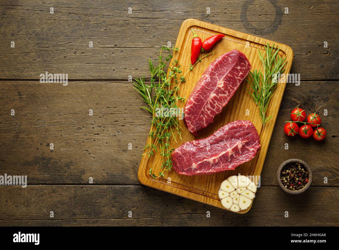 Au-dessus de deux steaks de bœuf à lame brute sur panneau de bois avec assaisonnements et herbes Banque D'Images