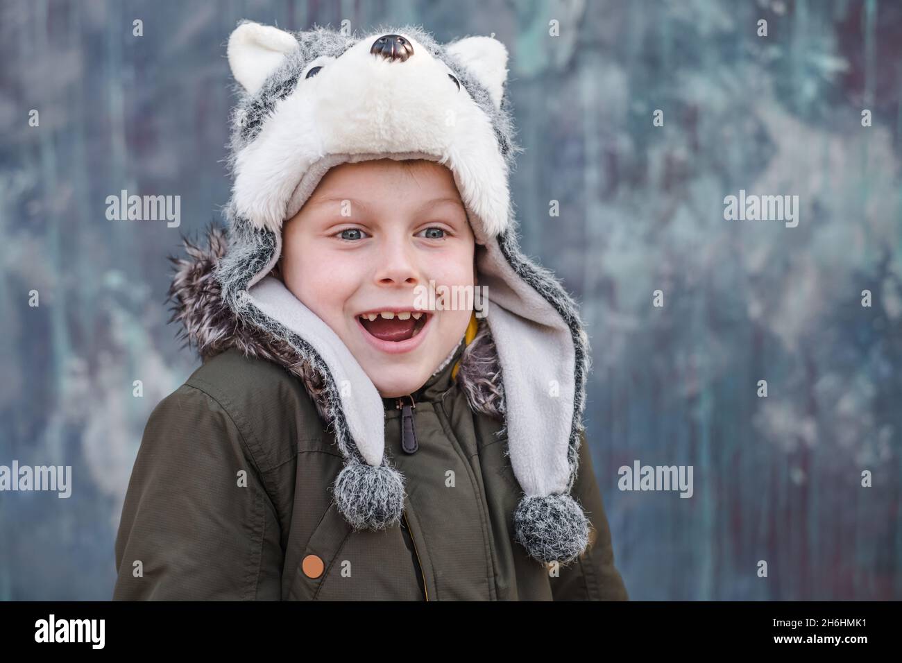 Portrait d'un enfant surpris dans un chapeau de loup et sourit doucement sur fond gris, extérieur. Espace pour le texte.Photo de haute qualité Banque D'Images