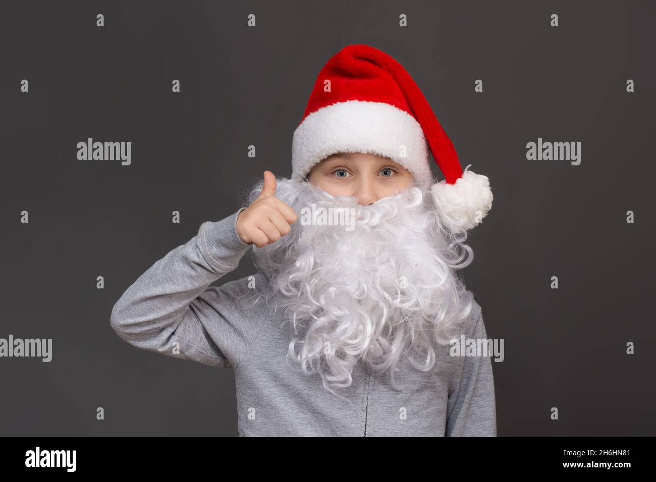 Portrait d'un garçon avec une barbe et un chapeau de père Noël montre la classe, pouces vers le haut. Banque D'Images