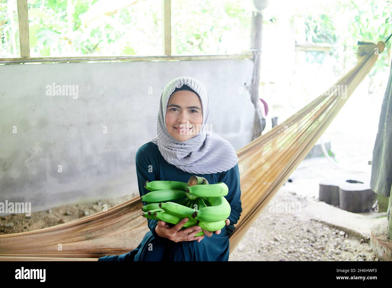 Femme musulmane assise sur un berceau en filet et tenant une bande de banane verte Banque D'Images