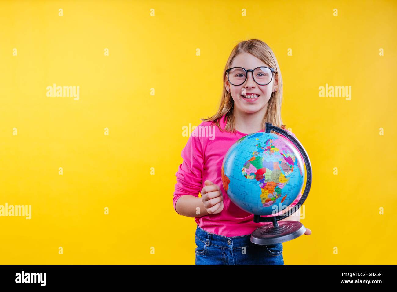Joyeux cheveux blond écolière avec lunettes de vue tenant le globe sur fond jaune avec espace vide pour le texte Banque D'Images