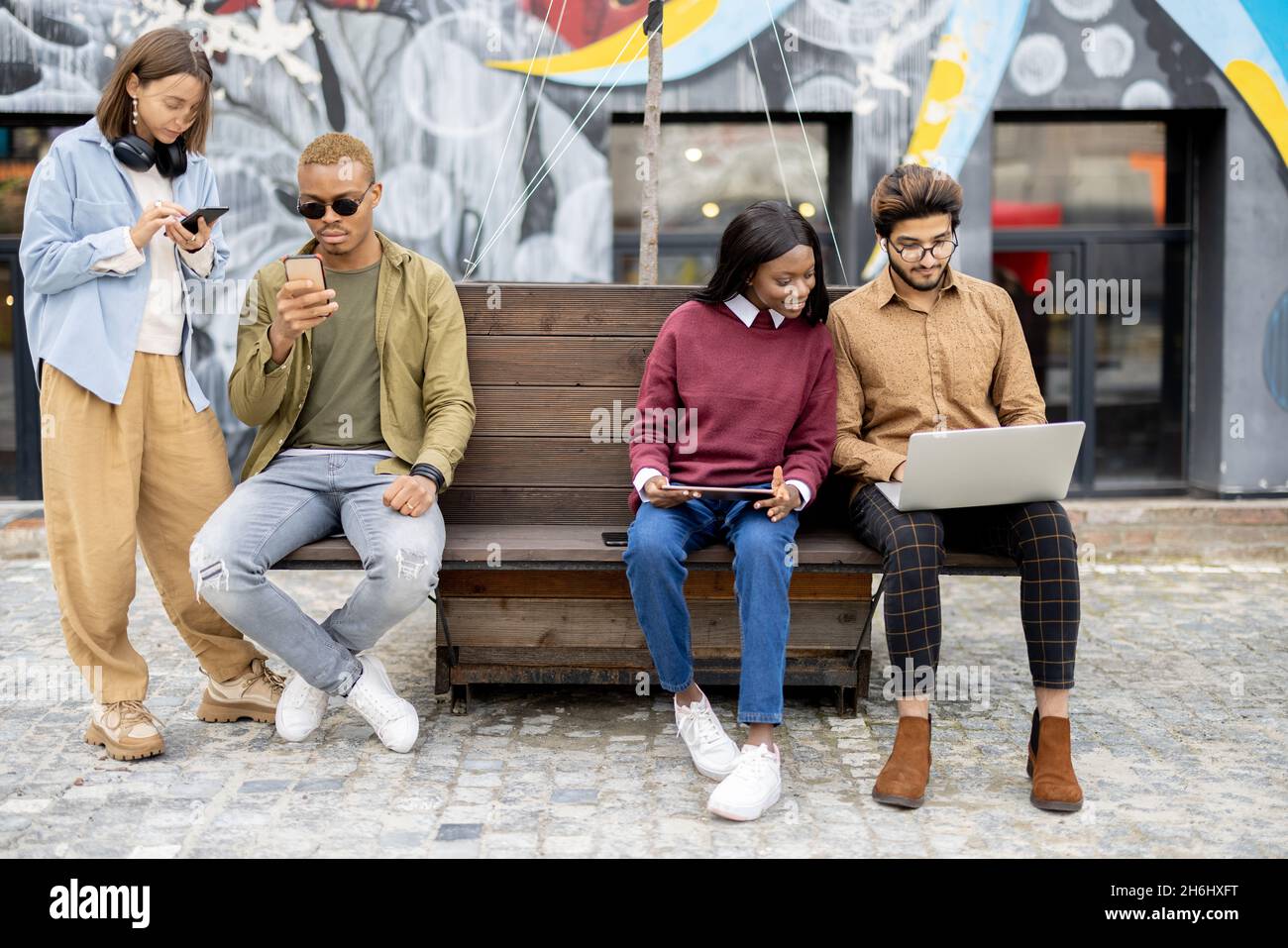 Étudiants utilisant des appareils numériques sur banc en bois Banque D'Images