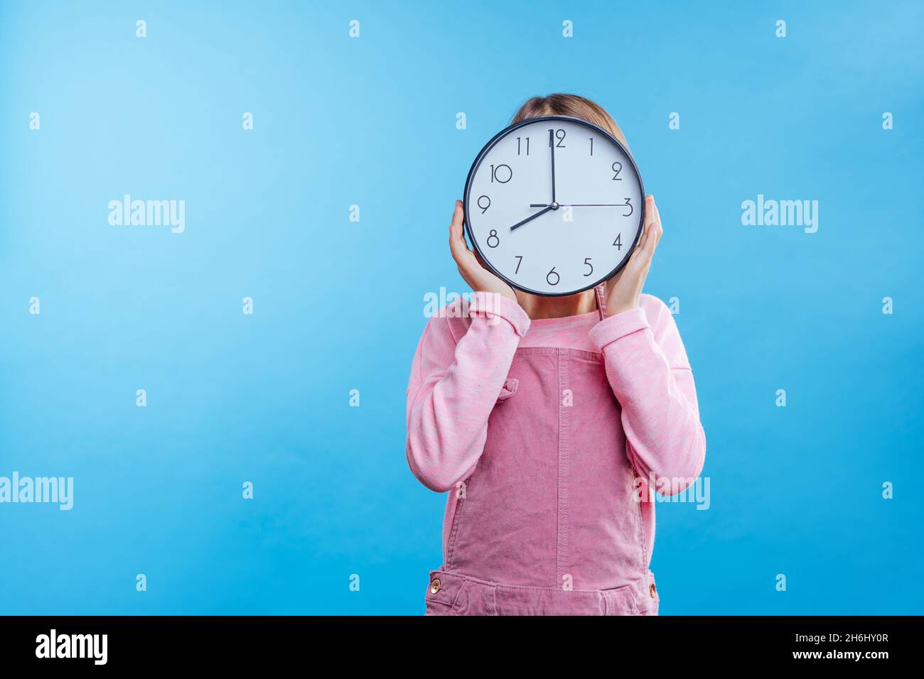 Petite fille tenant horloge sur fond bleu avec espace vide pour le texte.Bannière panoramique horizontale. Banque D'Images