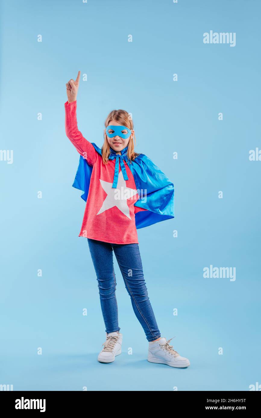 Petite fille portant le costume de super héros pointant vers le haut sur fond bleu avec espace vide pour le texte. Banque D'Images