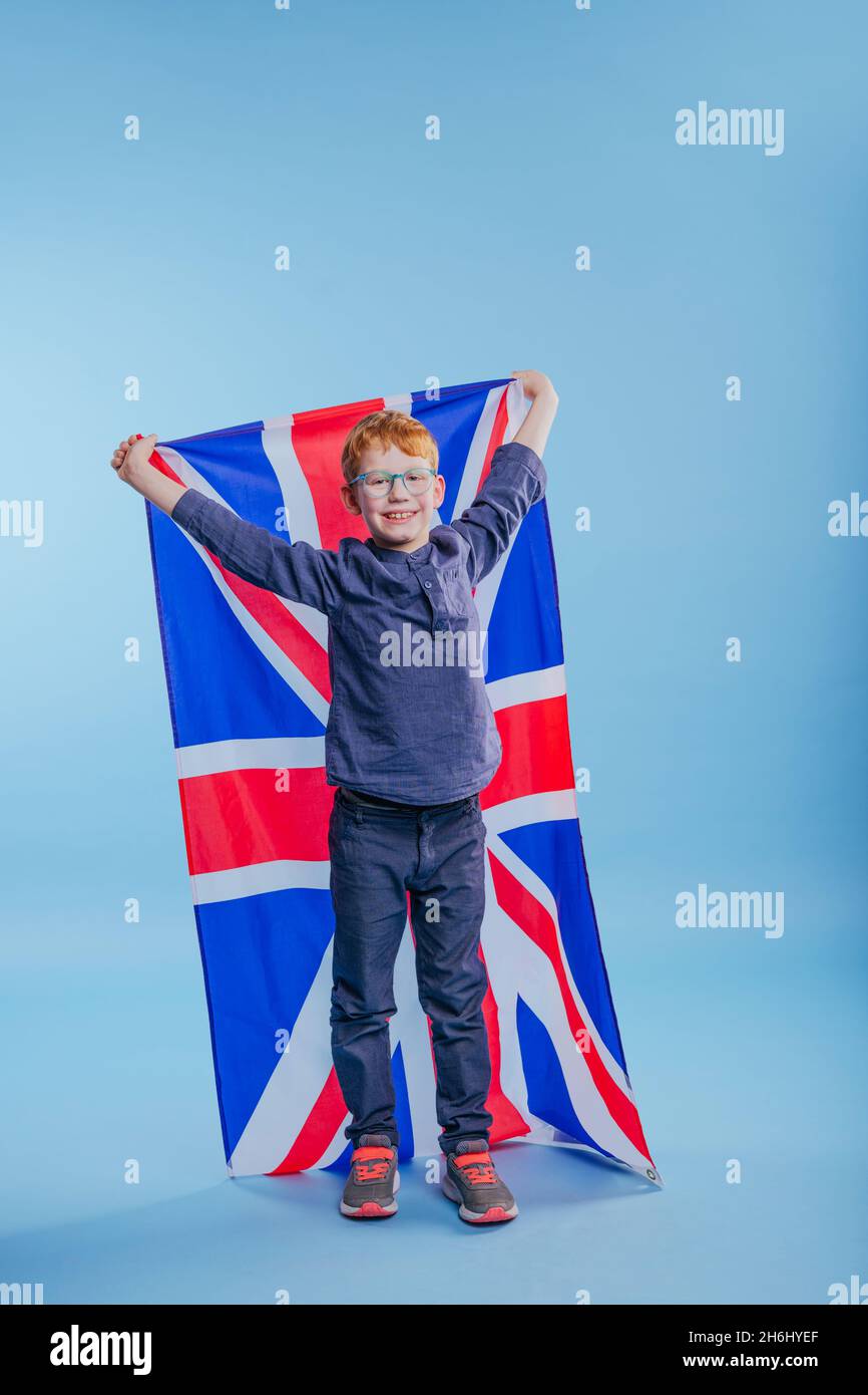 Un écolier portant des lunettes tenant le drapeau Jack de l'Union de Grande-Bretagne sur fond bleu avec un espace vide pour le texte Banque D'Images