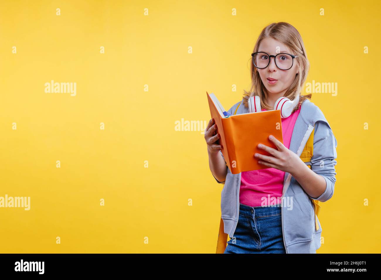 Bonne adolescente tenant sac à dos livre de lecture.Portrait de studio sur fond jaune avec espace vide pour le texte. Banque D'Images