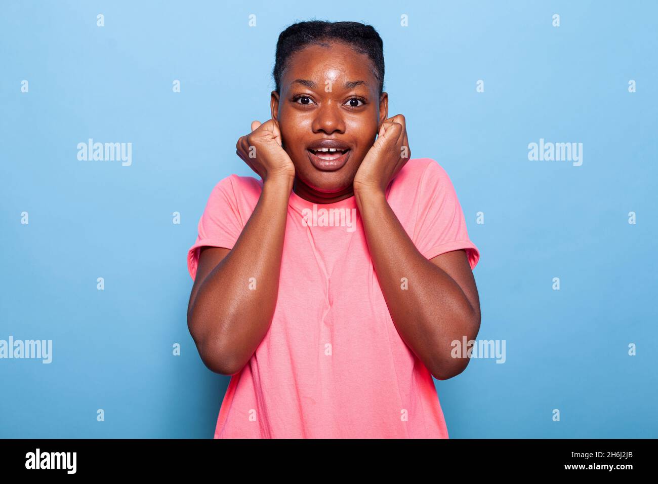 Portrait d'une jeune femme afro-américaine excitée souriant à l'appareil photo tout en se tenant en studio sur fond bleu.Adolescent ayant l'énergie de faire des expressions du visage joyeux.Concept de confiance Banque D'Images
