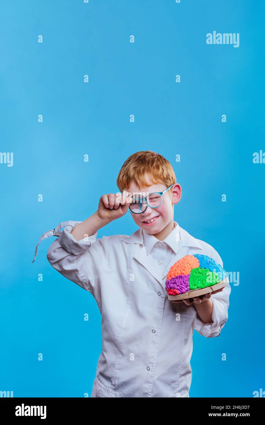 Garçon portant des lunettes et une robe de protection tenant le modèle de cerveau sur fond bleu avec un espace vide pour le texte Banque D'Images