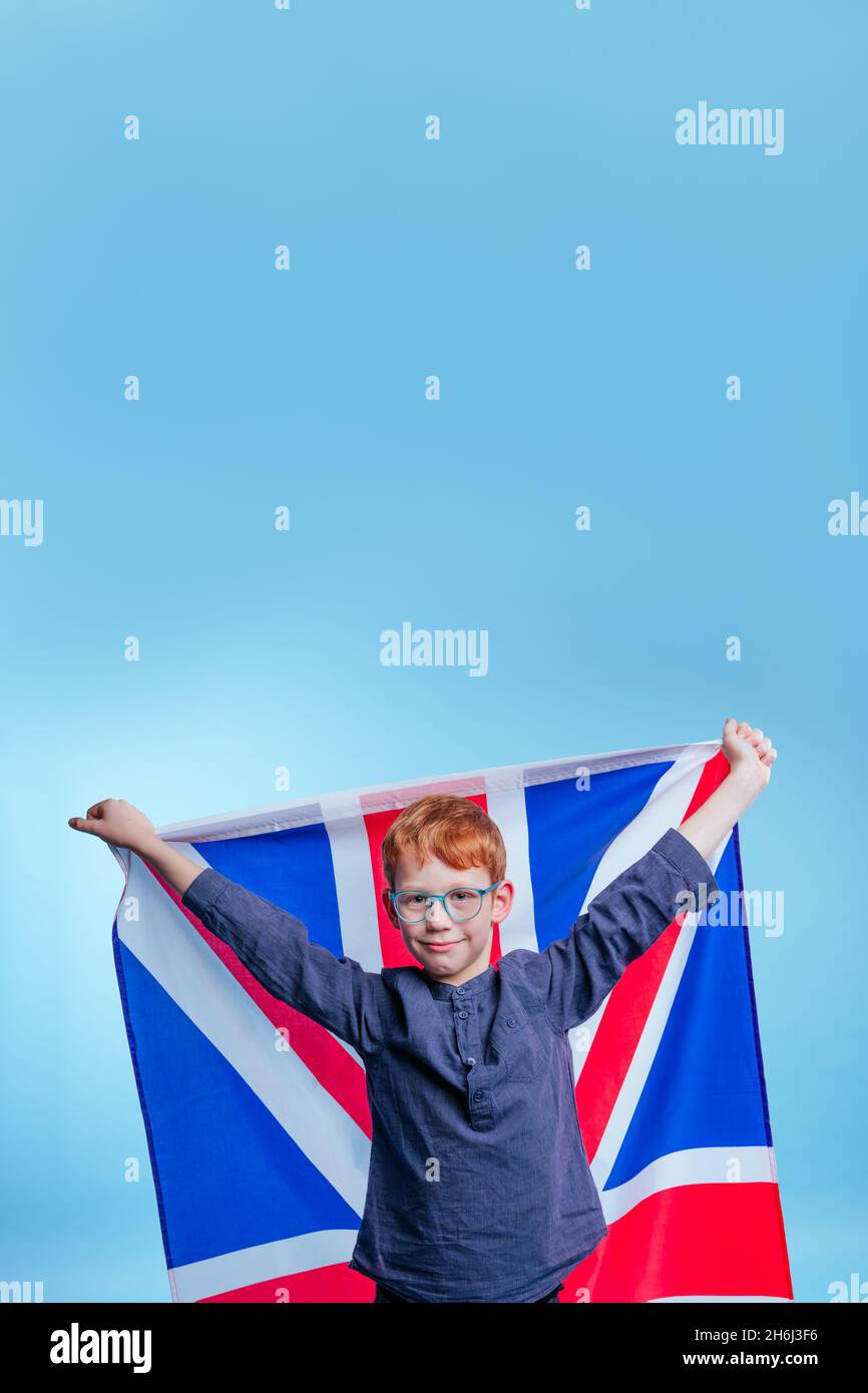 Un écolier portant des lunettes tenant le drapeau Jack de l'Union de Grande-Bretagne sur fond bleu avec un espace vide pour le texte Banque D'Images