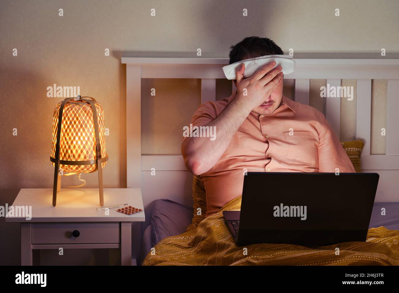 Homme malade adulte tenant sa tête avec honte sur le lit avec ordinateur Banque D'Images