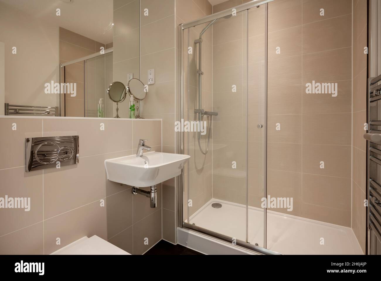 Cambridge, Angleterre - août 6 2019 : salle de bains/douche moderne partiellement carrelée avec lavabo en céramique mural, porte-serviettes, cabine de douche et grand miroir Banque D'Images