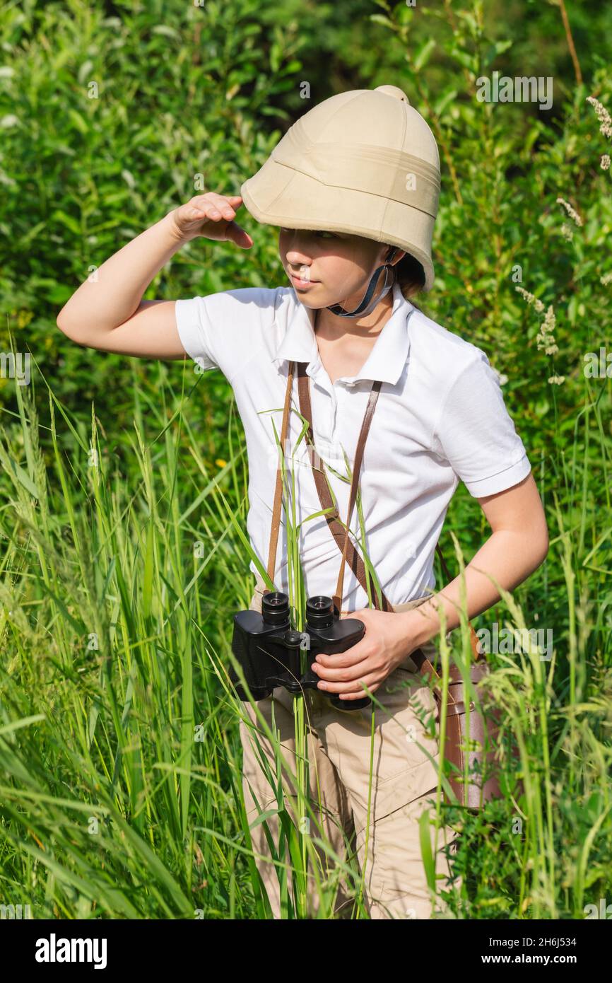 La préadolescente portant un casque en liège se tient dans les pairs de l'herbe dans la distance tenant sa main à ses yeux.Concept de découverte Banque D'Images