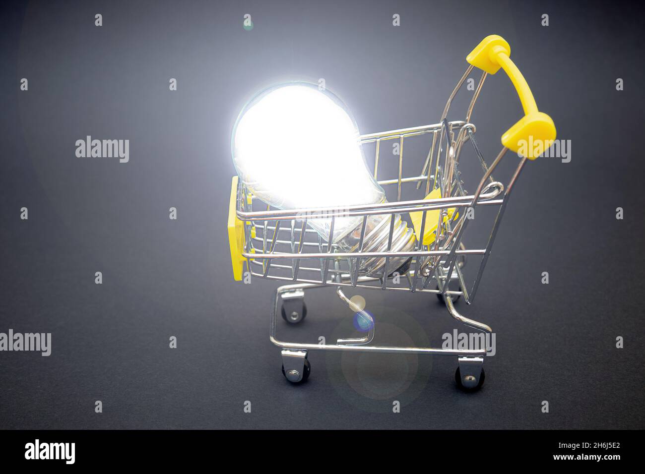 Ampoule à économie d'énergie dans un panier miniature sur fond gris.Le concept de mise à niveau vers les ampoules LED. Banque D'Images